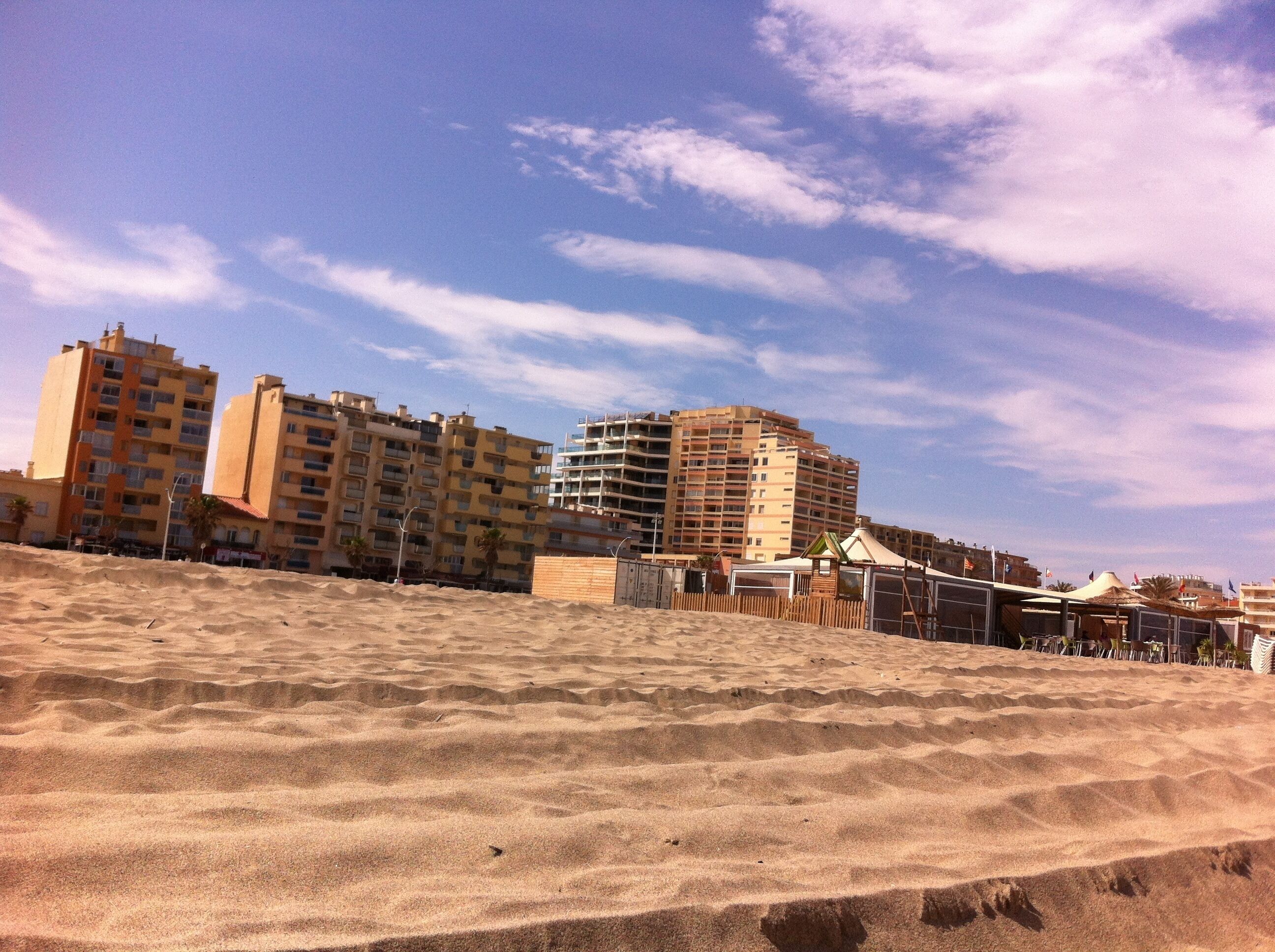 A sandy beach with buildings in the background.