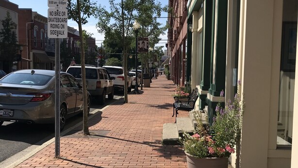 A brick-paved sidewalk with parked cars and a two-hour parking sign.