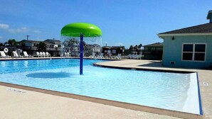 Une piscine avec un élément décoratif aquatique aux eaux verdoyantes, des chaises longues et un petit bâtiment en arrière-plan.