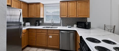 Una cocina moderna con armarios de madera, electrodomésticos de acero inoxidable, lavavajillas y microondas.