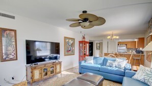 A living room with a television, blue sofa, ottoman, and a ceiling fan.