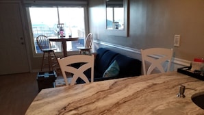 Una cocina con encimera de mármol, sillas blancas, una mesa de comedor y vista al exterior a través de un amplio ventanal.