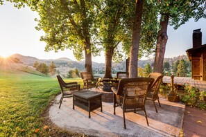 Un patio al aire libre con mobiliario de mimbre, un hogar para fogata y vistas del paisaje circundante.