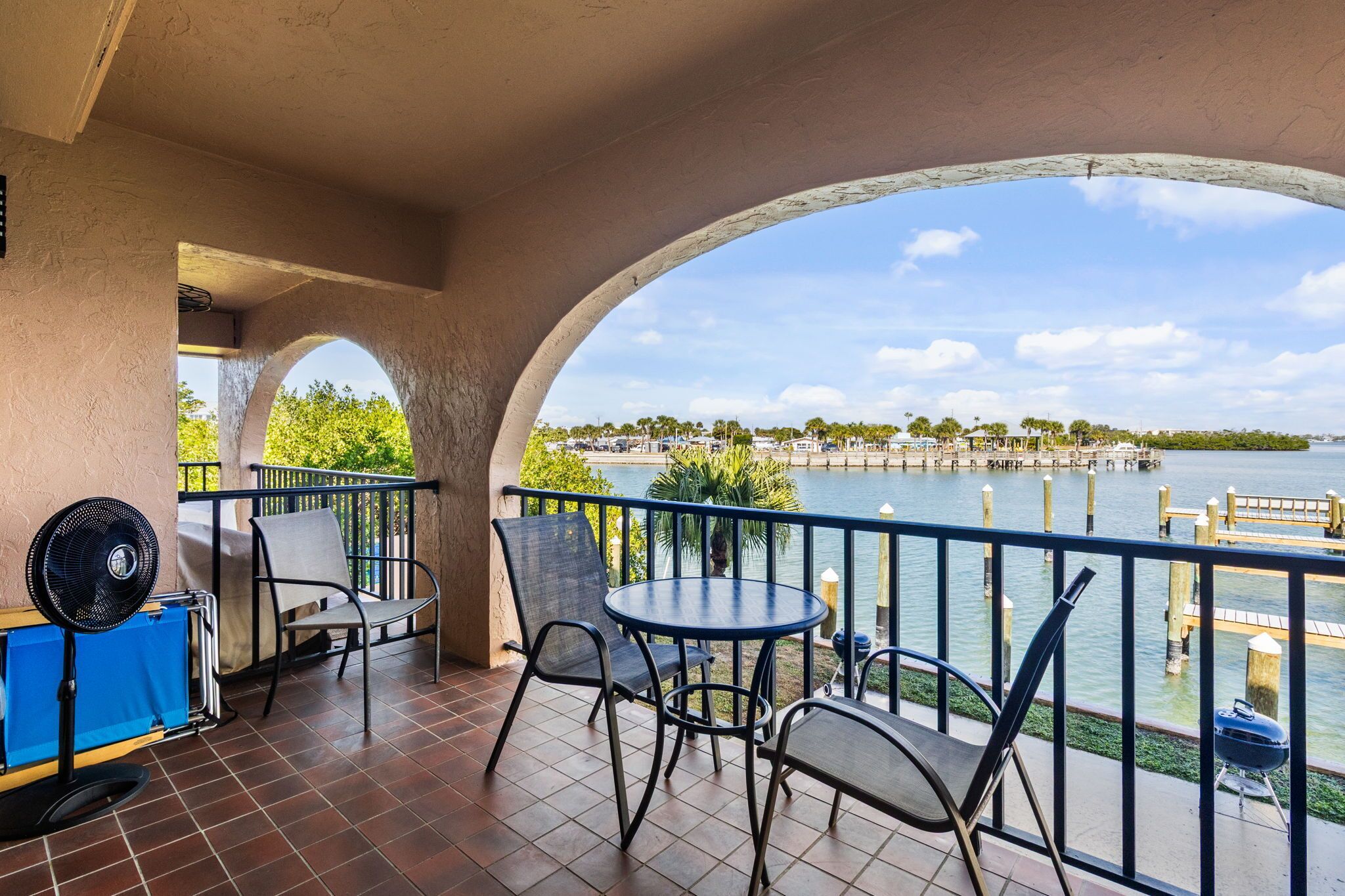 A balcony with outdoor seating, a grill, and a view of a lake with docks.