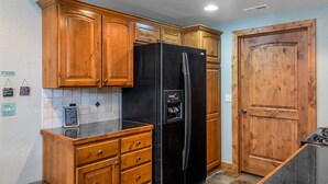 Eine Küche mit Holzausstattung, einem schwarzen Kühlschrank und einer gefliesten Rückwand.