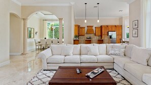 A spacious living room with a large L-shaped sectional sofa, a wooden coffee table, and a dining area with a chandelier.