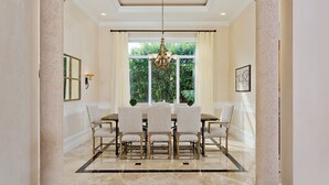 A dining room with a marble floor, a chandelier, and a view of greenery through large windows.