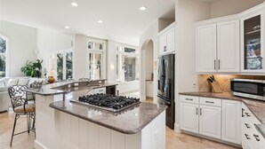 A modern kitchen with white cabinetry, a central island with a gas stove, and a stainless steel refrigerator. - Luxury 6BR 3rd Row Home w/ Patio & Private Pool (Hilton Head Island)