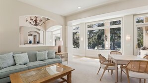 A spacious living room with a light blue sofa, a wooden coffee table, and a dining area with wicker chairs. - Luxury 6BR 3rd Row Home w/ Patio & Private Pool (Hilton Head Island)