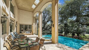 An outdoor patio with a pool, covered seating, and a dining area with chairs and a table. - Luxury 6BR 3rd Row Home w/ Patio & Private Pool (Hilton Head Island)