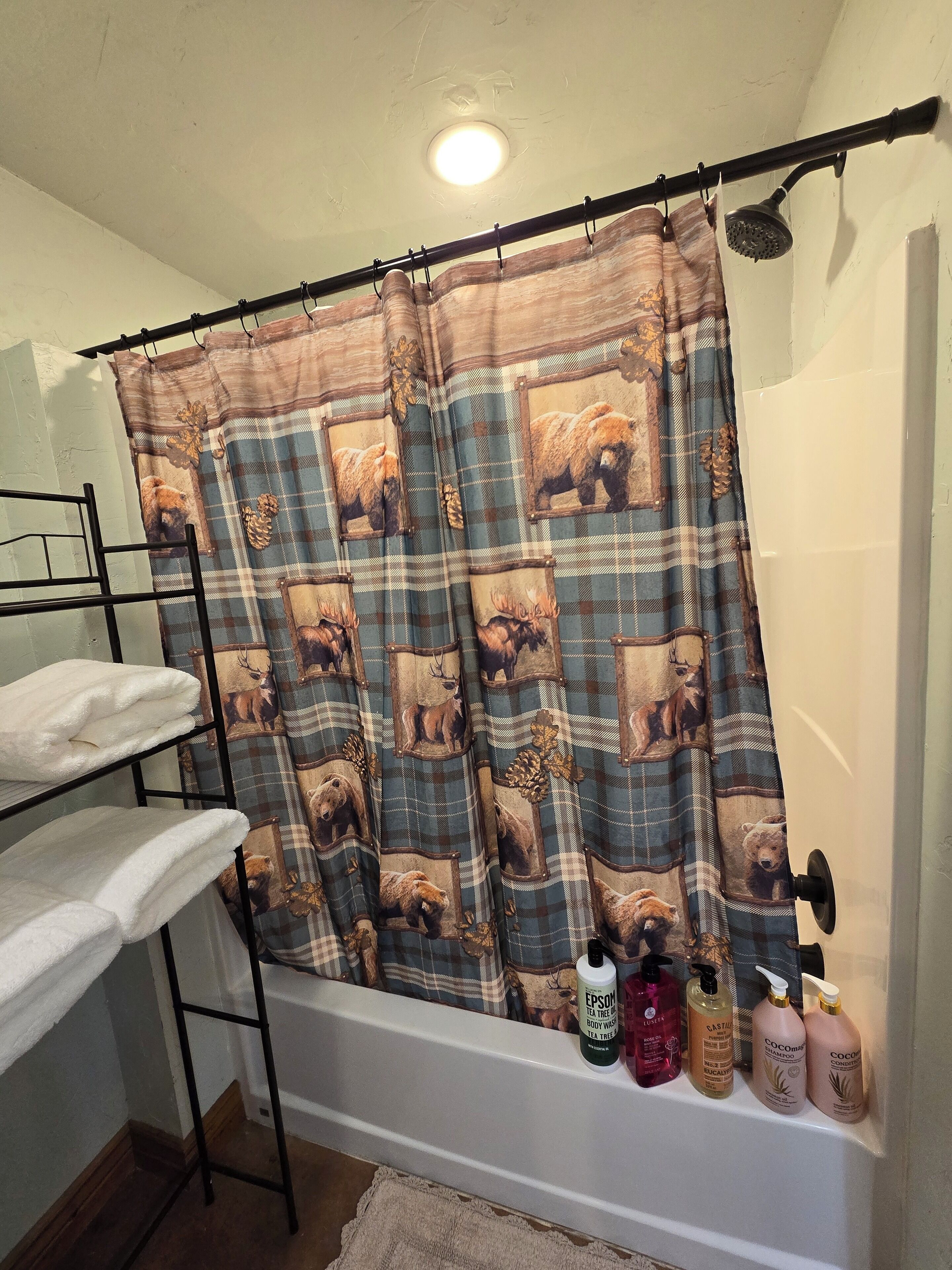 A bathroom with a shower curtain featuring bear and deer designs, a towel rack with towels, and toiletries on a shelf.