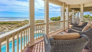 Espaço coberto ao ar livre com móveis de vime e piscina, com vista para a praia e o oceano.