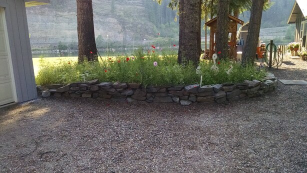 A garden area with a stone border, trees, and a wooden structure. - A Cabin On The River<br>Three days minimum<br>Closed from October 15th to April 1 (Troy)