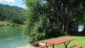 A picnic table with benches, a fire pit, and a view of a lake surrounded by trees. - A Cabin On The River<br>Three days minimum<br>Closed from October 15th to April 1 (Troy)