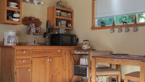 A kitchen with wooden cabinets, a microwave, a coffee maker, and a window with a view of greenery. - A Cabin On The River<br>Three days minimum<br>Closed from October 15th to April 1 (Troy)