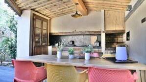Un área de cocina al aire libre con una mesa de madera, sillas y plantas en macetas.