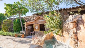 Una cabaña rústica de madera con un muro de piedra y una pequeña cascada.