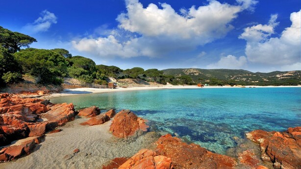 Un paisaje costero con aguas turquesas cristalinas, formaciones rocosas y una playa de arena.