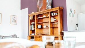 Un coin repas avec un buffet en bois, un tableau représentant des verres à vin et un réfrigérateur blanc.