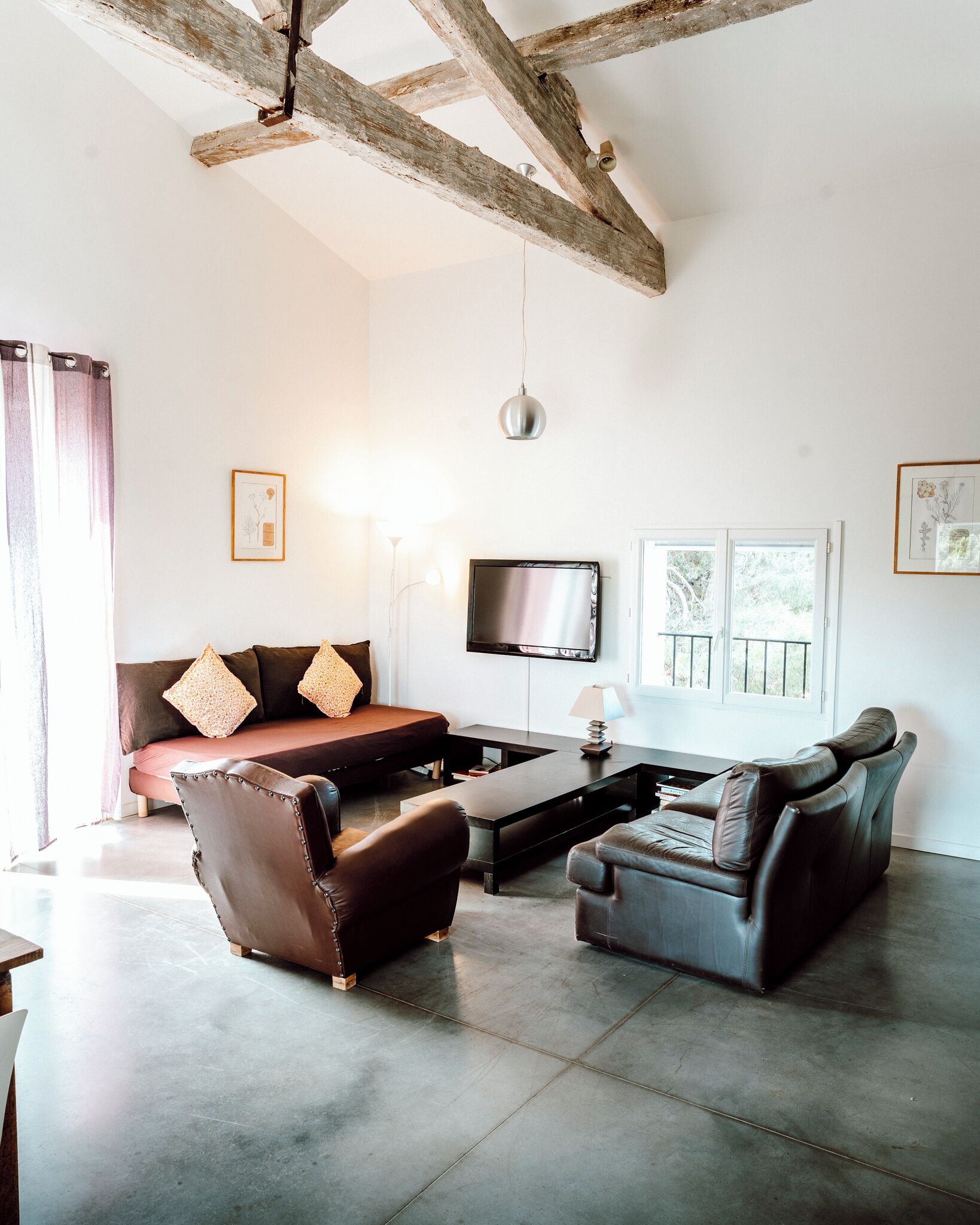A living room with a sofa, two armchairs, a coffee table, a TV, and a ceiling with exposed beams.