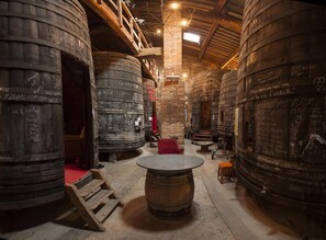 A rustic interior with large wooden barrels, a central round table, and a staircase leading to an upper level. - Authentic, charming farmhouse in the heart of a winegrowing estate with sea views (Canet-En-Roussillon)