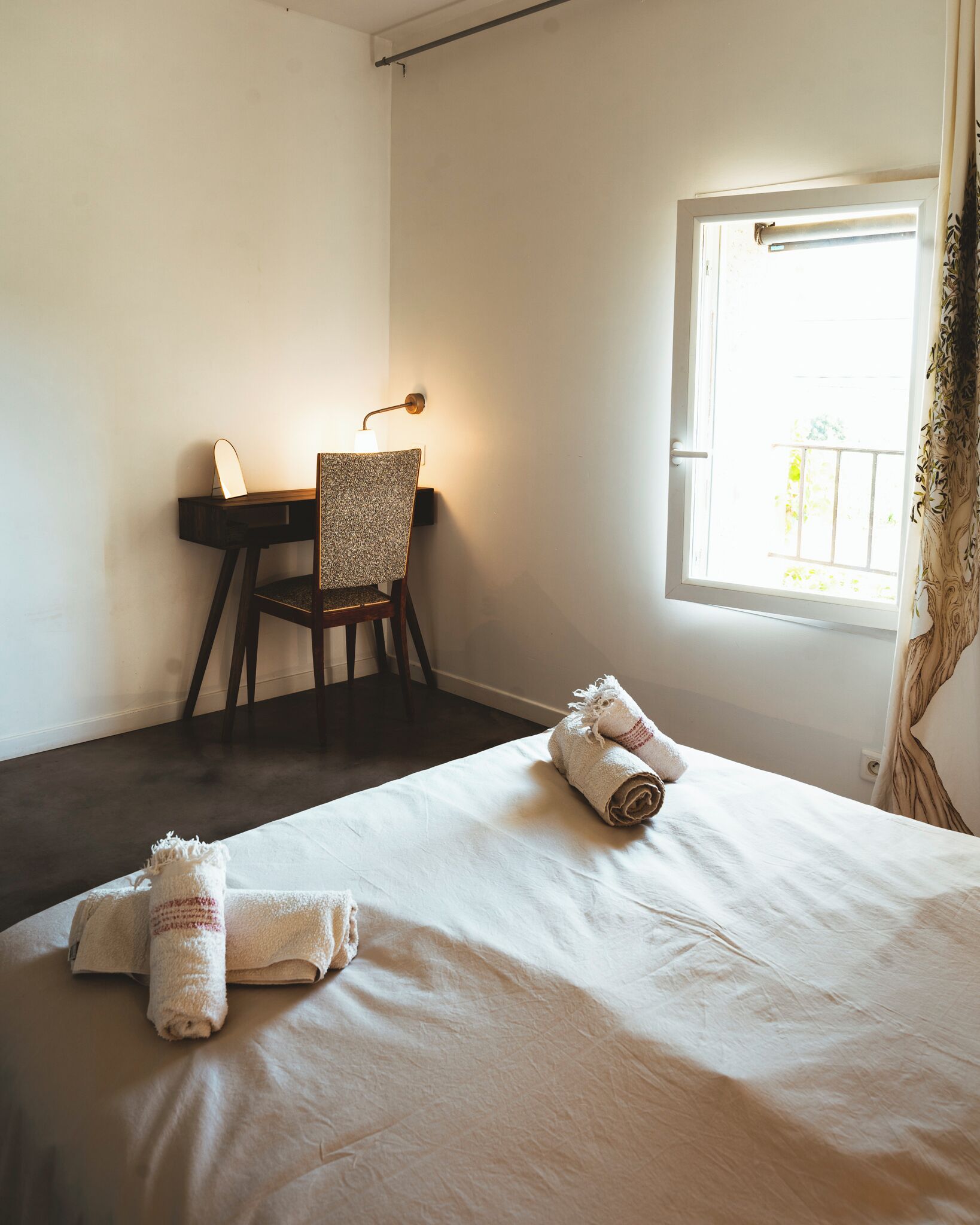 A hotel room with a bed, a desk, and a chair. There are towels on the bed and a window with curtains.