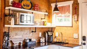 A kitchen with wooden walls, a white microwave, and a coffee maker. - SWEET HILL COUNTRY CABIN in the PERFECT location;  Sleeps 4-5 (Dripping Springs)
