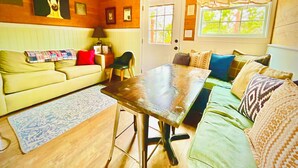 A cozy living room with a wooden ceiling, a sofa, a coffee table, and a window with curtains. - SWEET HILL COUNTRY CABIN in the PERFECT location;  Sleeps 4-5 (Dripping Springs)