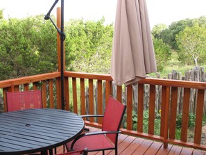 A wooden deck with a round table and two chairs, a pergola with a canopy, and a view of greenery in the background. - SWEET HILL COUNTRY CABIN in the PERFECT location;  Sleeps 4-5 (Dripping Springs)