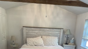 Une chambre à coucher avec un grand lit, une tête de lit en bois, une table de chevet avec une lampe et une fenêtre avec des stores.