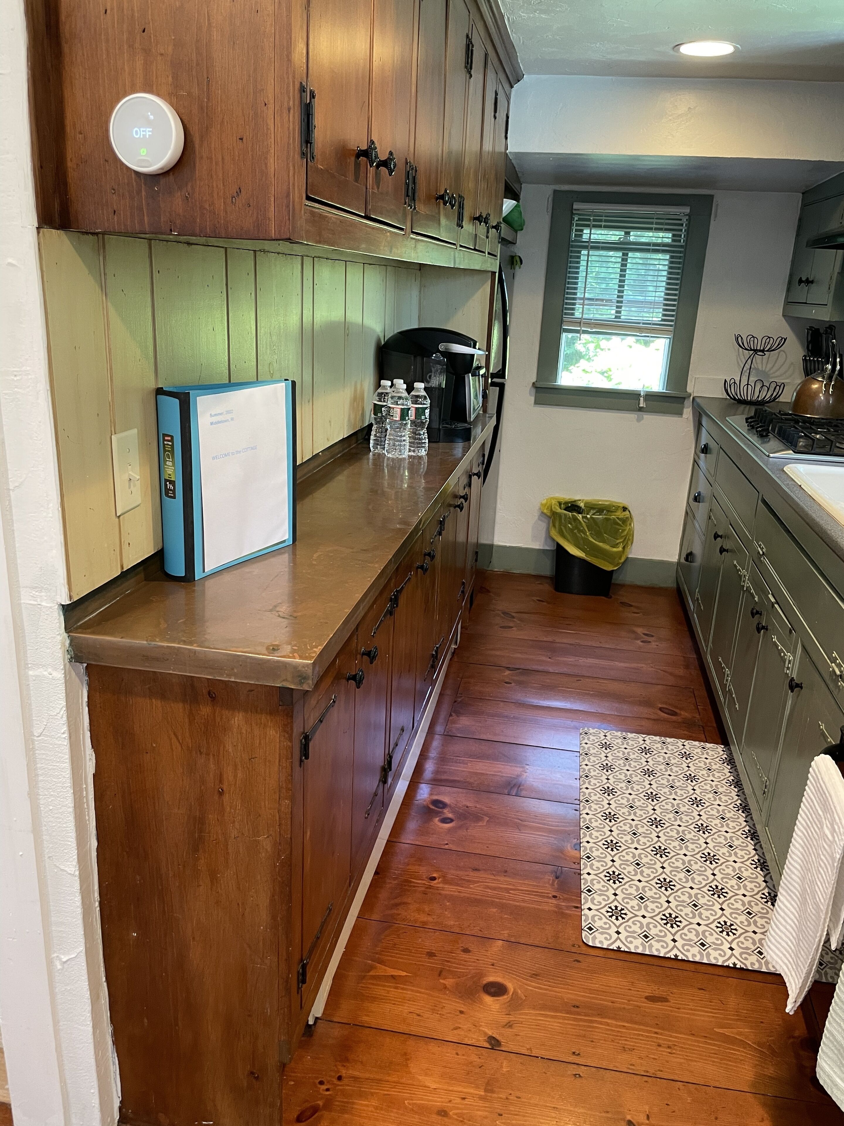 A kitchen with wooden cabinets, a built-in oven, a coffee maker, and a window with blinds.