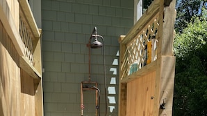 Un espace de douche extérieur en bois, comprenant un banc, un tuyau d’arrosage et une clôture en bois.