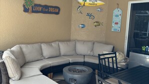 A cozy living area with a curved sectional sofa, a round fire pit, a dining table with chairs, and a ceiling fan.