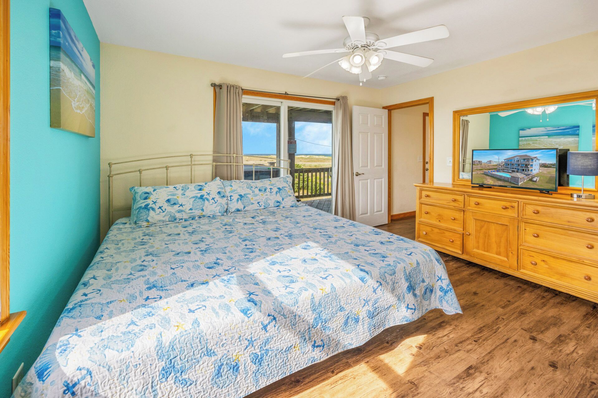 A bedroom with a bed, a dresser, a ceiling fan, and a large window with curtains.