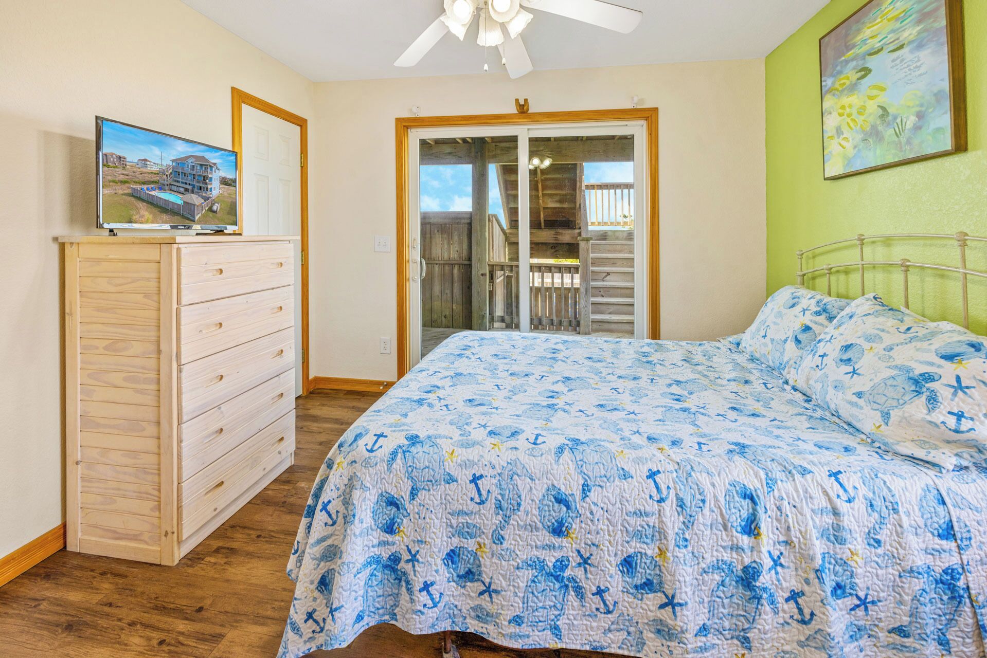 Une chambre à coucher avec un lit, une commode, un ventilateur de plafond et une vue sur un balcon.