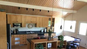 A modern kitchen with wooden cabinets, a central island with plants, a microwave, and a sink. - Country Living in the City (Bozeman)