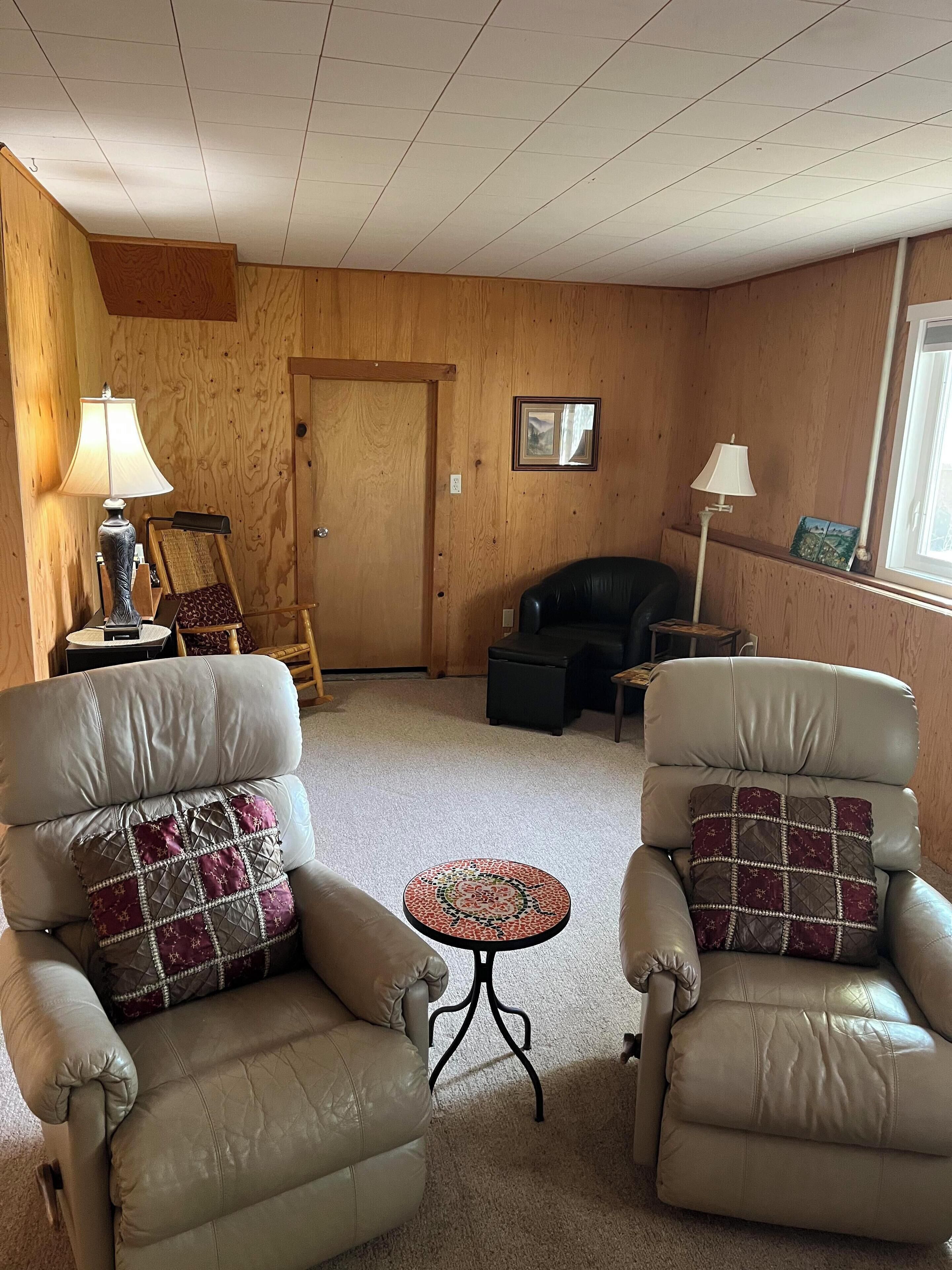 A living room with two leather armchairs, a small round table, and a wooden door.