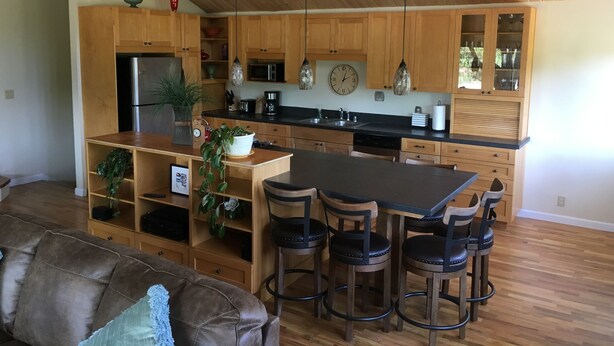 A modern kitchen with wooden cabinets, a central island with bar stools, a refrigerator, and a clock on the wall. - Country Living in the City (Bozeman)