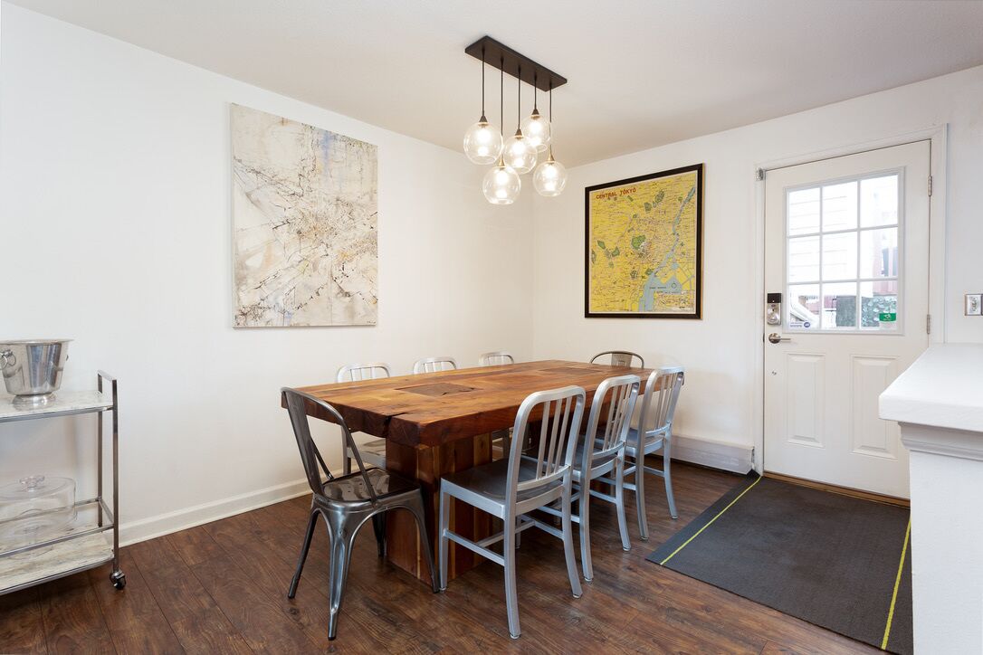 Un coin repas avec une table en bois, des chaises en métal, une carte accrochée au mur et un chariot muni d’un récipient en métal.
