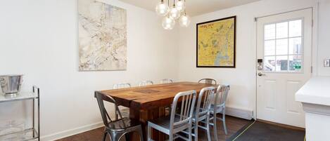 Un coin repas avec une table en bois, des chaises en métal, une carte accrochée au mur et un chariot muni d’un récipient en métal.