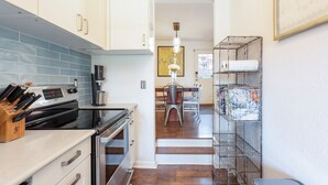 Una cocina moderna con armarios blancos, salpicadero de azulejos azules, electrodomésticos de acero inoxidable y un comedor con candelabro.