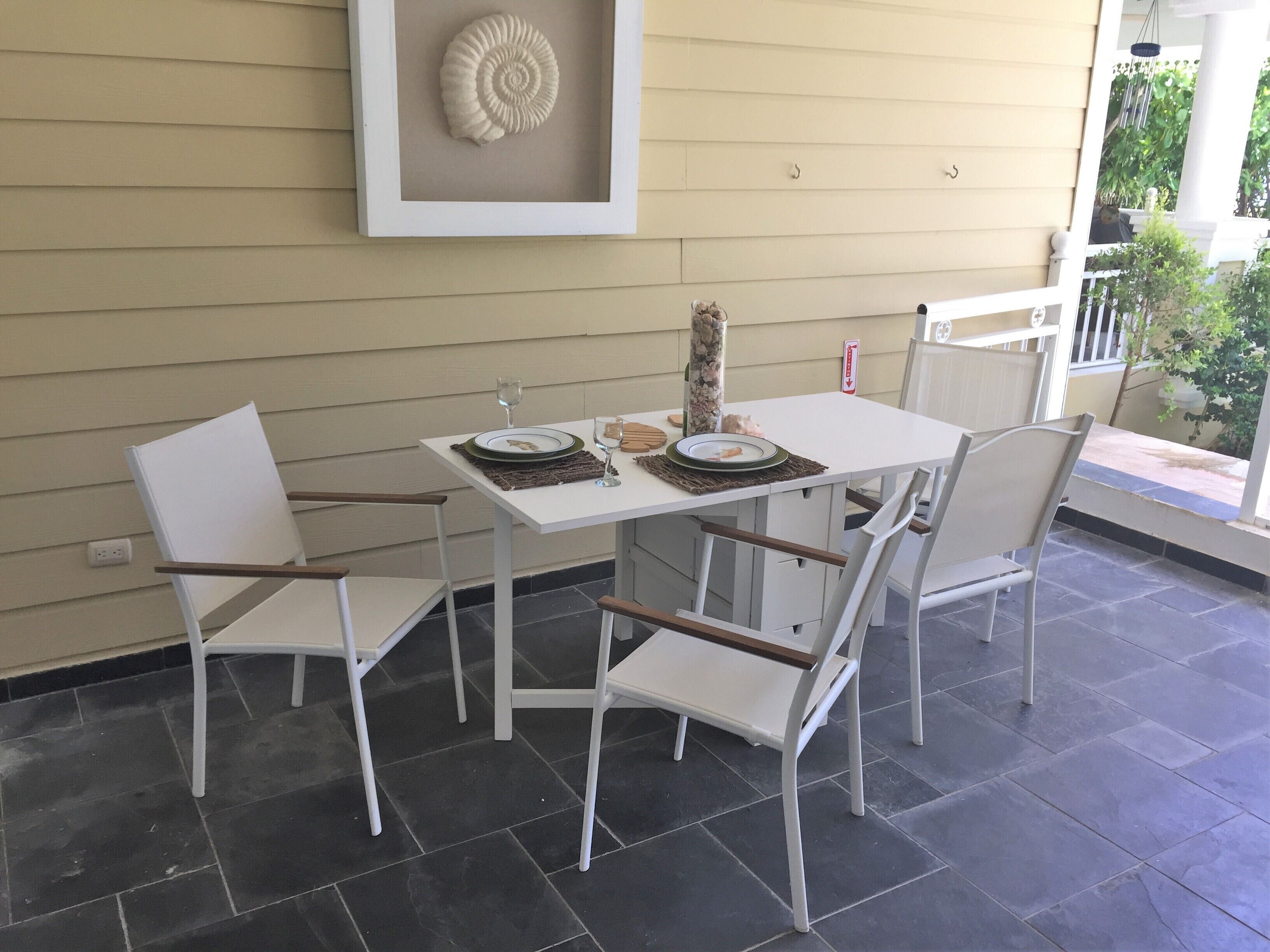 A dining area with a white table and chairs, a framed fossil on the wall, and a view of greenery outside.