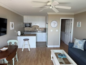 A living room with a dining area, kitchen, and a ceiling fan.