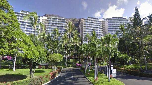 A hotel with multiple high-rise buildings, a well-maintained garden with palm trees, and a clear sky.