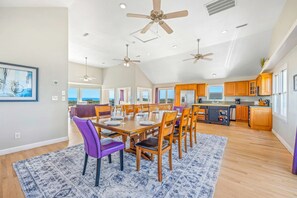 Une salle à manger spacieuse avec un plafond haut, plusieurs ventilateurs de plafond et une vue sur l’océan.