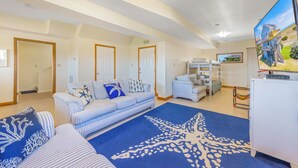 Un ampio soggiorno con un grande tappeto a forma di stella marina, un divano, letti a castello, una TV e vista sulla spiaggia.