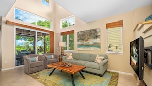 A spacious living room with a large window, a sofa, a coffee table, and a TV. - Hilton Waikoloa Pool Pass for stays in 2026/Waikoloa Golf Discounts (Waikoloa Beach Resort)