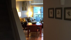 Een woonkamer met een bank, salontafel en een eethoek met stoelen en een tafel. Er hangen fotolijsten aan de muur.