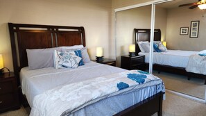 A double bed with floral bedding, a nightstand with a lamp, and a large mirror reflecting the room.
