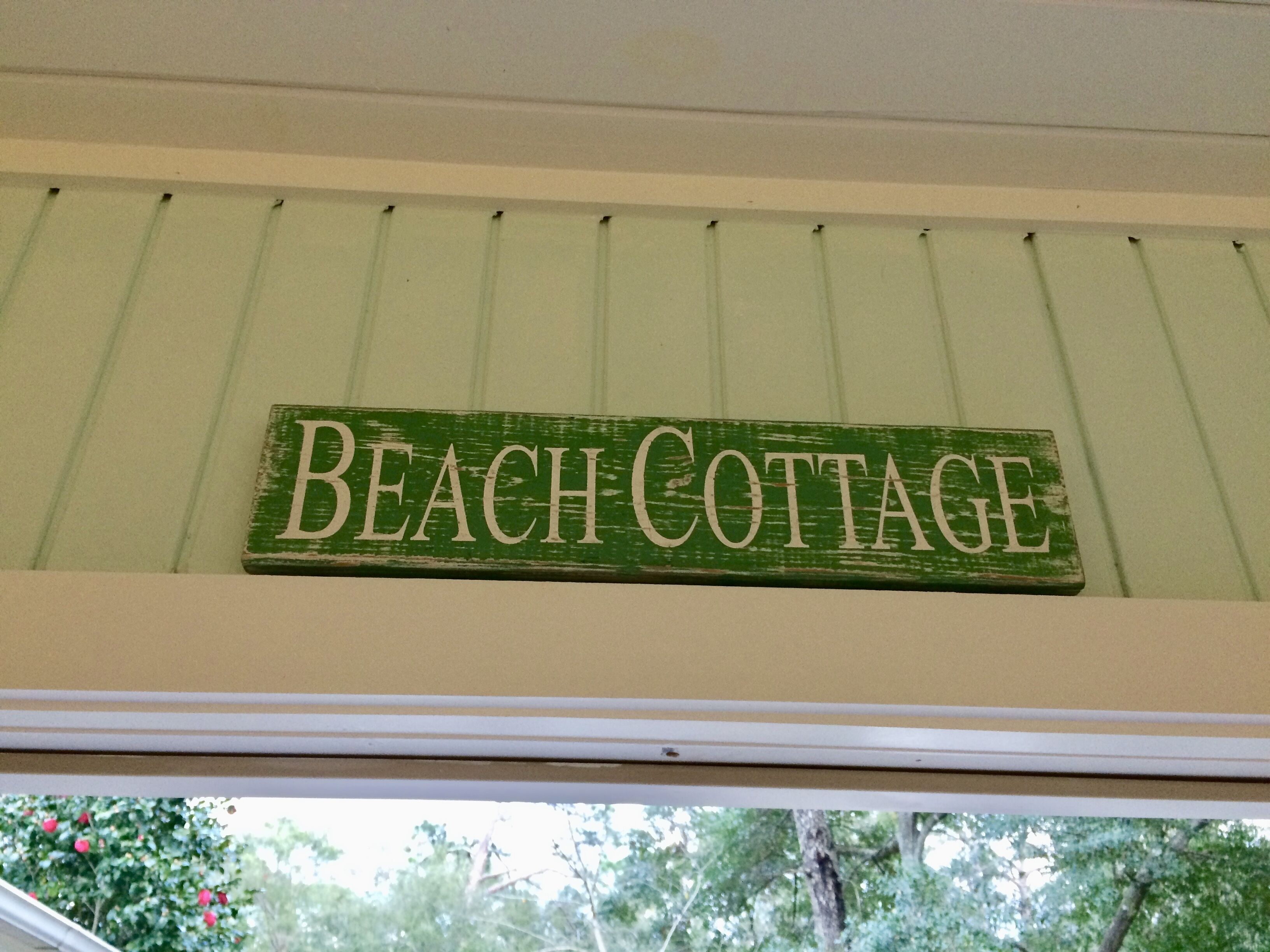 A green sign with white lettering reading "Beach Cottage" mounted on a white wall.